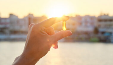 Hand holding translucent yellow pill against sun setting in background