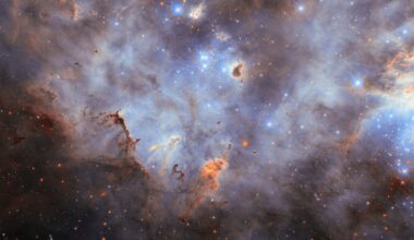Stars in a star cluster shine brightly blue, with four-pointed diffraction spikes radiating from them. The center shows a small, crowded group of stars while a larger group is partially visible on the right side of the image. The nebula is mostly thick, smoky clouds of gas, lit up in blue tones by the stars. Clumps of dust hover before and around the stars; they are mostly dark but lit around their edges where the starlight erodes them.