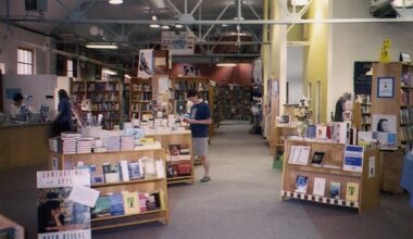 A large room filled with bookshelves and three people standing and reading.