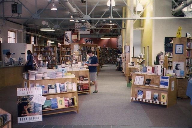 A large room filled with bookshelves and three people standing and reading.