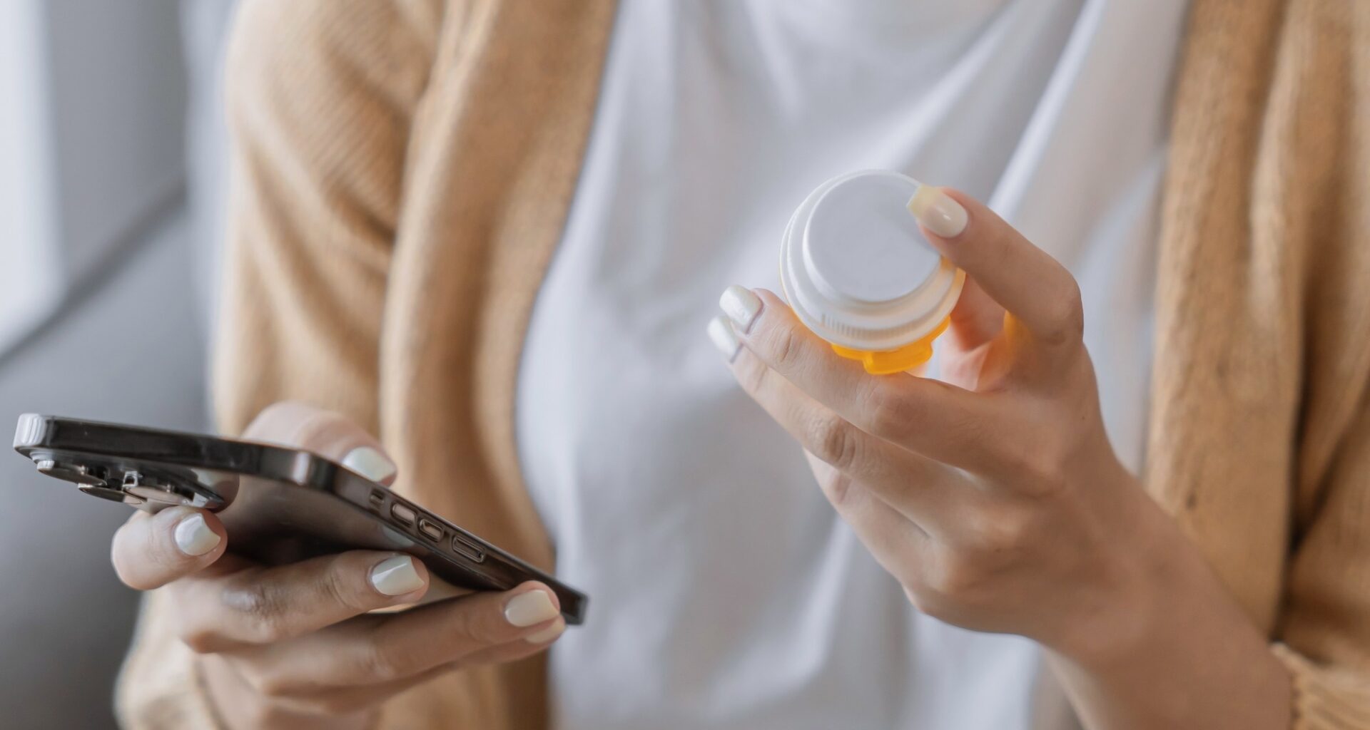 Woman reading information online on mobile phone holding bottled prescription drug