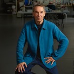 A man in a blue jacket sits in an art studio.