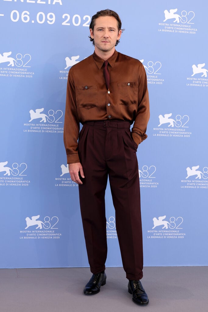 Lewis Pullman attends "The Testament Of Ann Lee" Venice Film Festival photocall Saint Laurent Brown shirt and trousers, Lewis Pullman Venice Film Festival 2025, Kaia Gerber Givenchy, Saint Laurent, The Testament Of Ann Lee