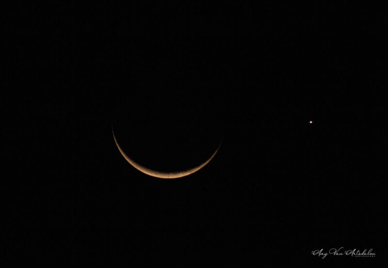 Slim crescent moon and one bright light beside it.