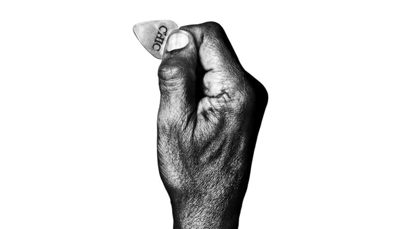 A close-up of a hand holding a guitar pick between the thumb and index finger against a white background.