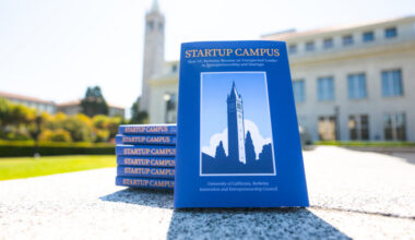 A copy of the Startup Campus book leans against a stack of six copies, with the Campanile blurred in the background