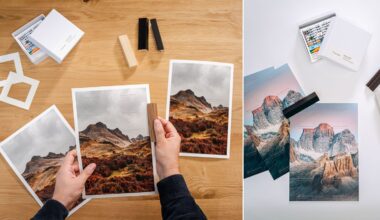 A person compares printed landscape photos on a wooden table, using color swatches. Nearby are art supplies, frames, and more prints, including mountain scenes and colored pencils in open boxes.