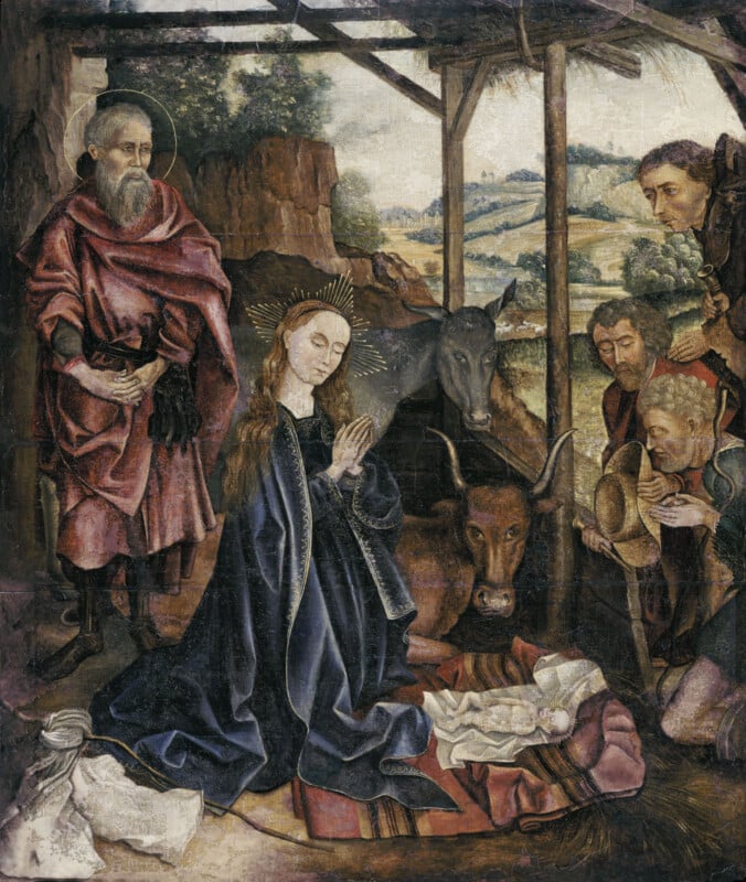 A nativity scene showing Mary and Joseph with baby Jesus in a manger, surrounded by onlookers, with a donkey and ox behind them in a rustic stable setting. Mary and Jesus have glowing halos.
