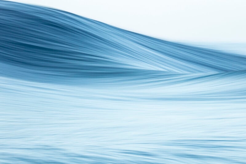A smooth, abstract image of a blue ocean wave, softly blurred, with gentle curves and flowing lines creating a sense of motion and tranquility. The scene is dominated by various shades of blue.
