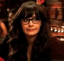 Person with long hair and glasses looks sideways, raising eyebrows humorously in a busy indoor setting