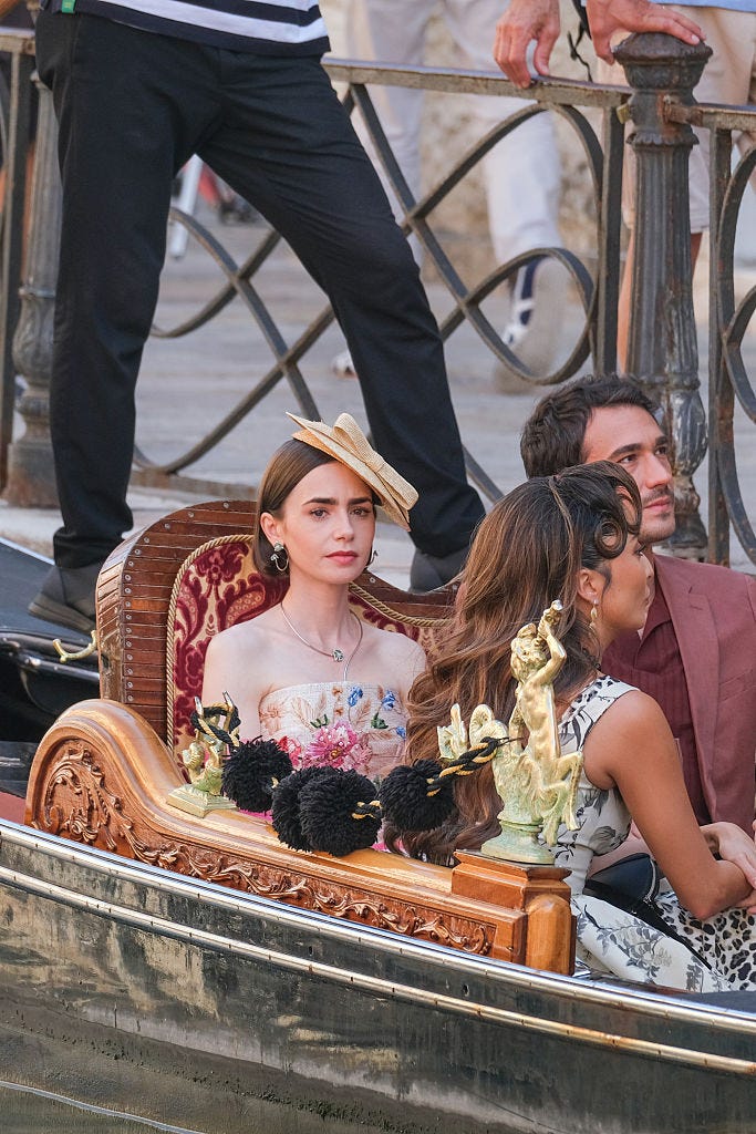 lily collins and eugenio franceschini in an elaborately carved venice canal boat from emily in paris set she is wearing a hat and embrouidered sleeveless dress lily collins and eugenio franceschini in an elaborately carved venice canal boat from emily in paris set she is wearing a hat and embrouidered sleeveless dress
