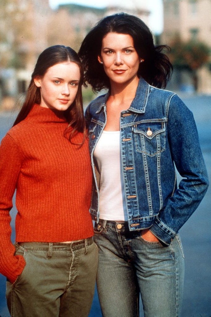 alexis bledel in red sweater and lauren graham in jean jacket standing on a street smiling in in gilmore girls promo pic alexis bledel in red sweater and lauren graham in jean jacket standing on a street smiling in in gilmore girls promo pic