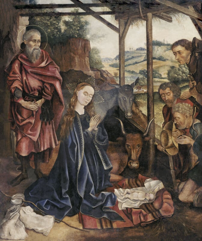 A nativity scene shows Mary praying over baby Jesus in a manger, surrounded by Joseph, three shepherds, an ox, and a donkey, with a rustic shelter and a rural landscape in the background.