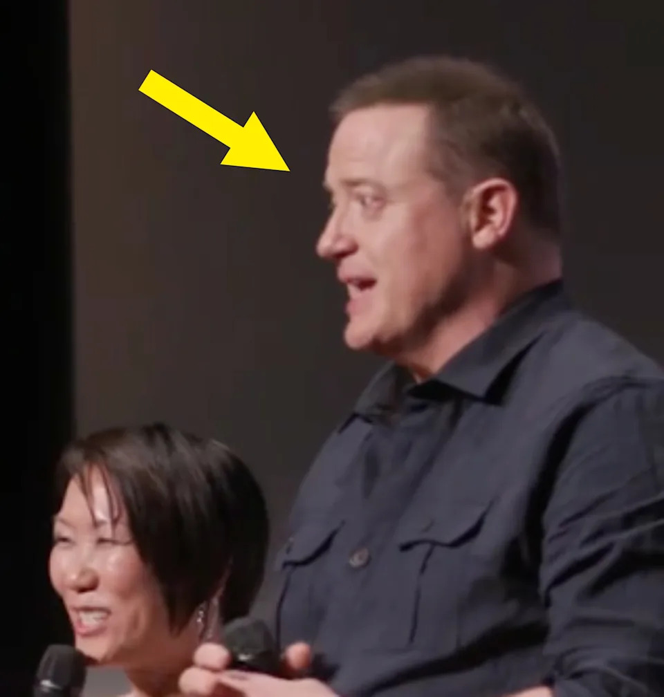 Two people holding microphones, engaged in conversation on stage. The person on the right is wearing a casual button-up shirt