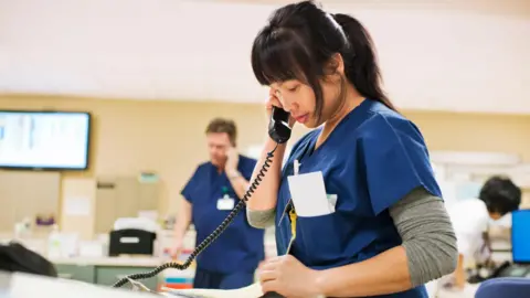 Getty Images Nurse in blue scrubs takes notes while on the phone
