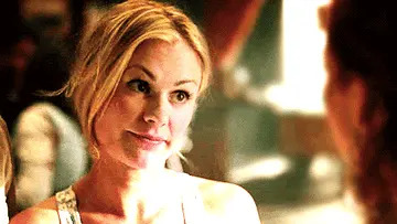 Person smiling, wearing a casual sleeveless top, with hair tied back, engaging in a conversation with someone off-camera