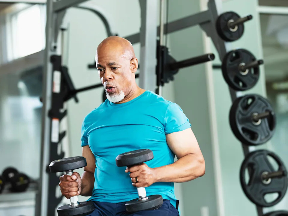 A senior African-American man working out at the gym, lifting dumbbells.