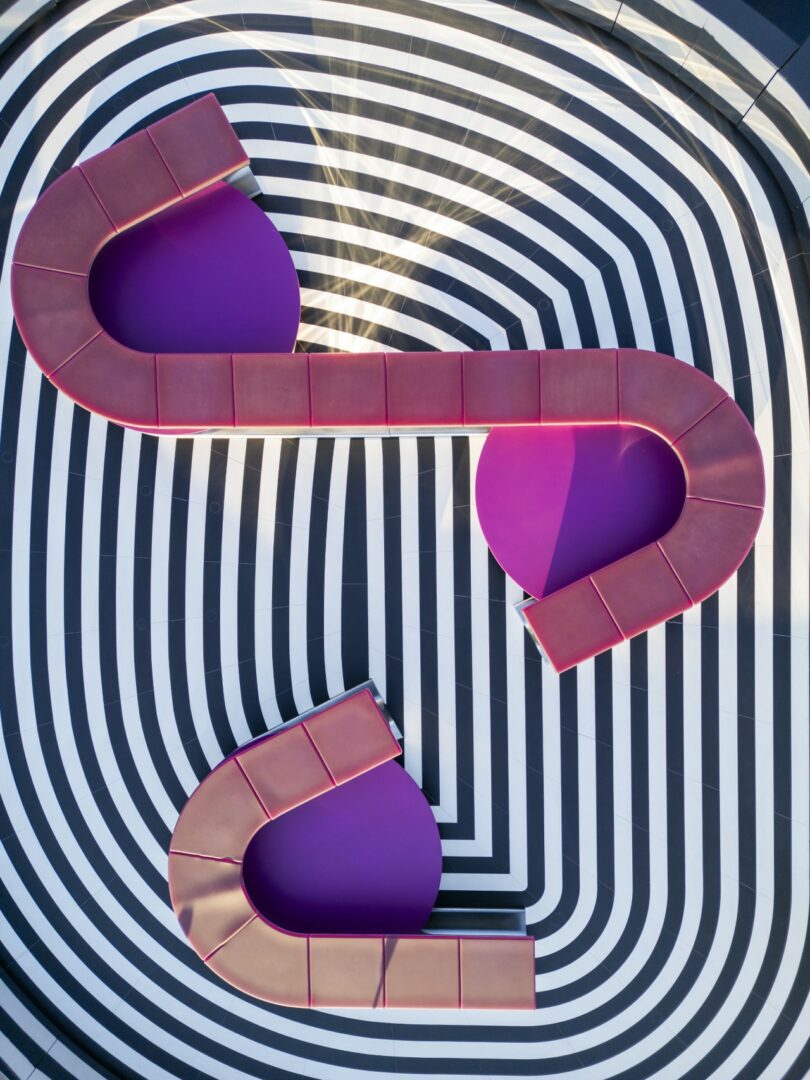 Aerial view of two curved, purple benches on a black and white concentric oval striped floor