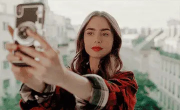 Person taking a selfie with a calm cityscape in the background, wearing casual plaid attire