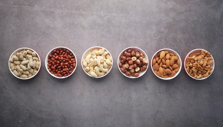 5 bowls of different nuts, including unshelled peanuts.
