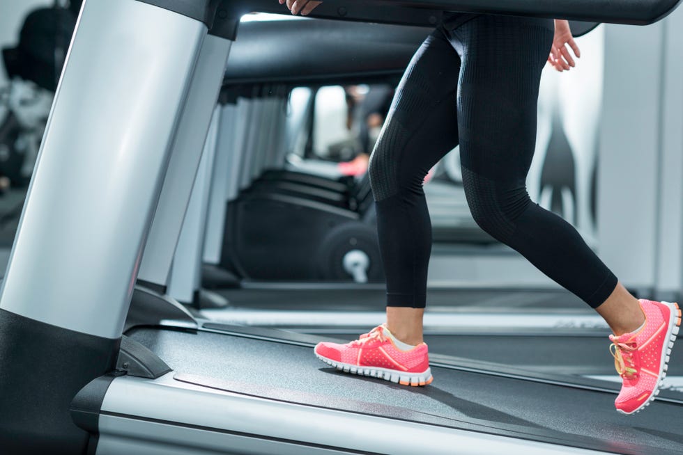 Incline Treadmill Running woman using incline threadmill in modern gym. incline threadmills are used to simulate uphill walking or running and deliver additional workout benefits to users. woman is wearing black yoga pants andrunning sports shoes.