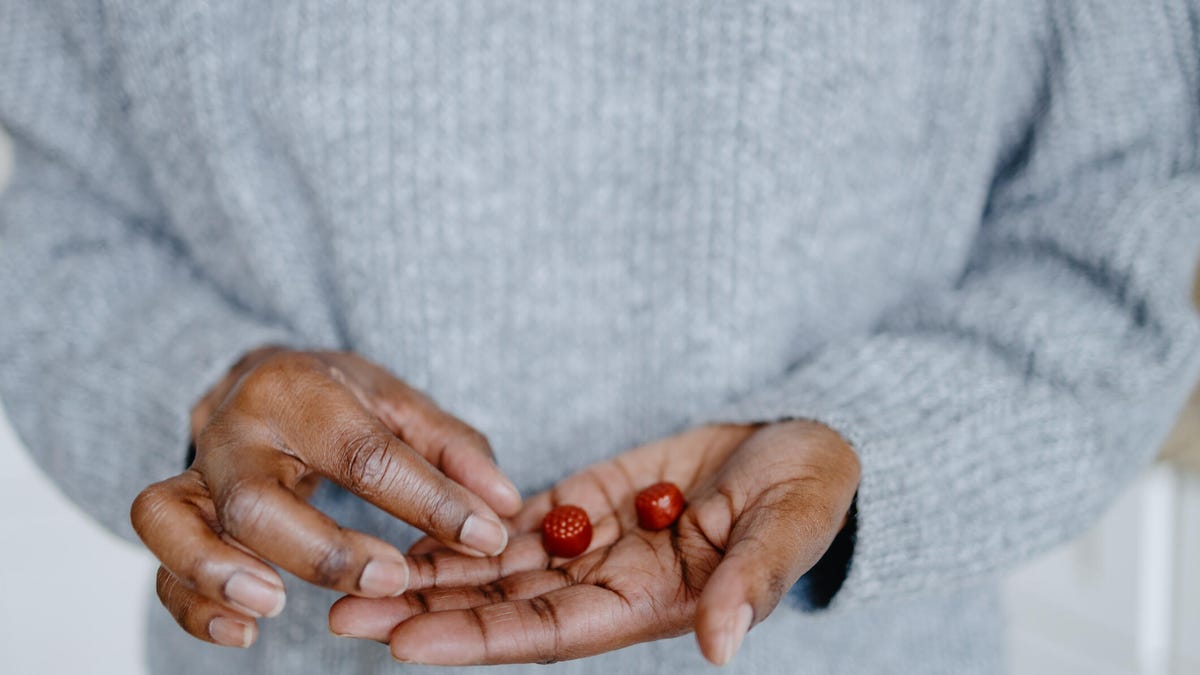 A close up of a person&apos;s hand holding two red gummy supplements. They are wearing a light grey sweater.