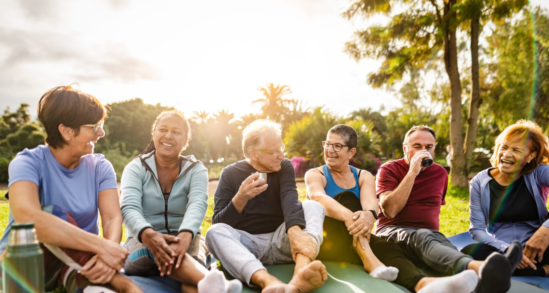 Happy multiracial senior friends drinking a tea after workout activities in a park