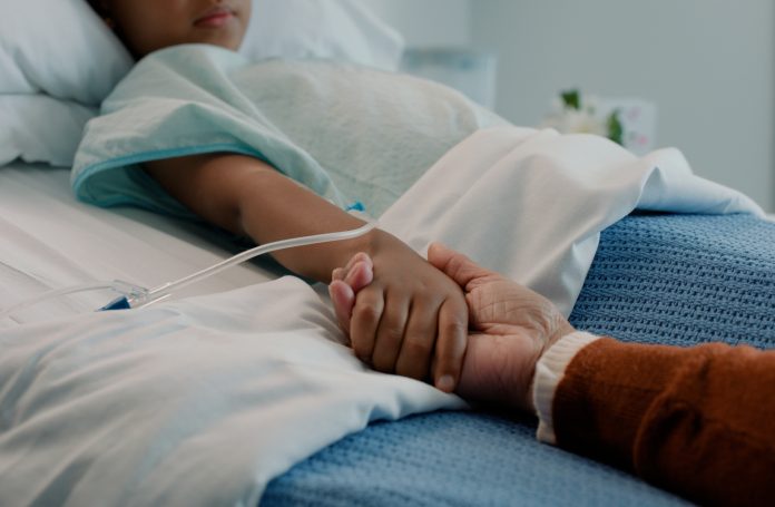 Hospital, holding hands and kid in bed with love, support and care in clinic after surgery. Child, healthcare and cancer patient with empathy, kindness and caregiver with compassion with help