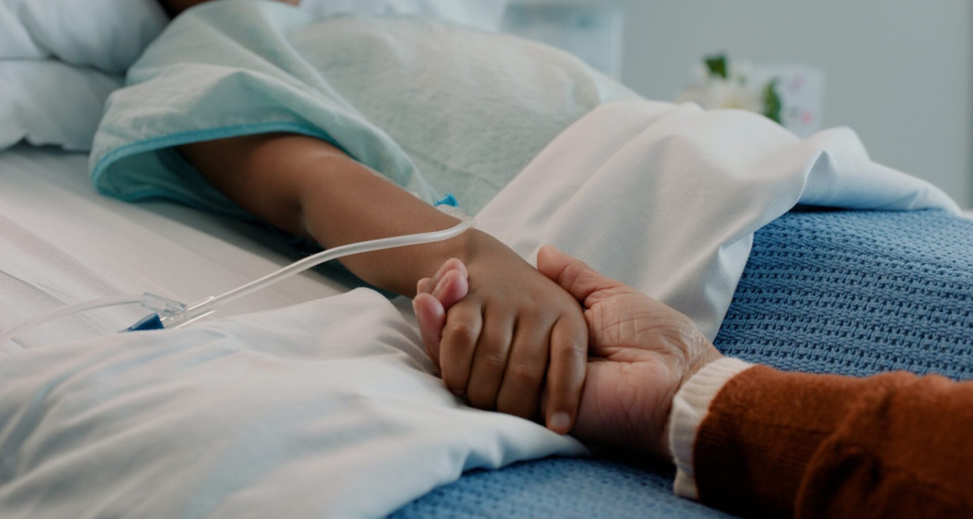 Hospital, holding hands and kid in bed with love, support and care in clinic after surgery. Child, healthcare and cancer patient with empathy, kindness and caregiver with compassion with help