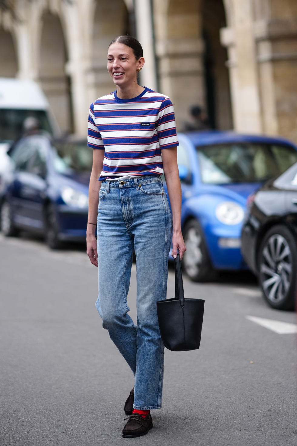 paris, france june 19: a guest wears gold earrings, white blue and red striped t shirt, light blue high waisted denim jean pants, black bucket leather bag, red socks, brown loafer suede shoes, outside lemaire, during the paris fashion week menswear spring/summer 2025 on june 19, 2024 in paris, france. (photo by edward berthelot/getty images)