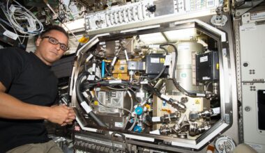 Astronaut in glasses working with scientific equipment inside an International Space Station laboratory.