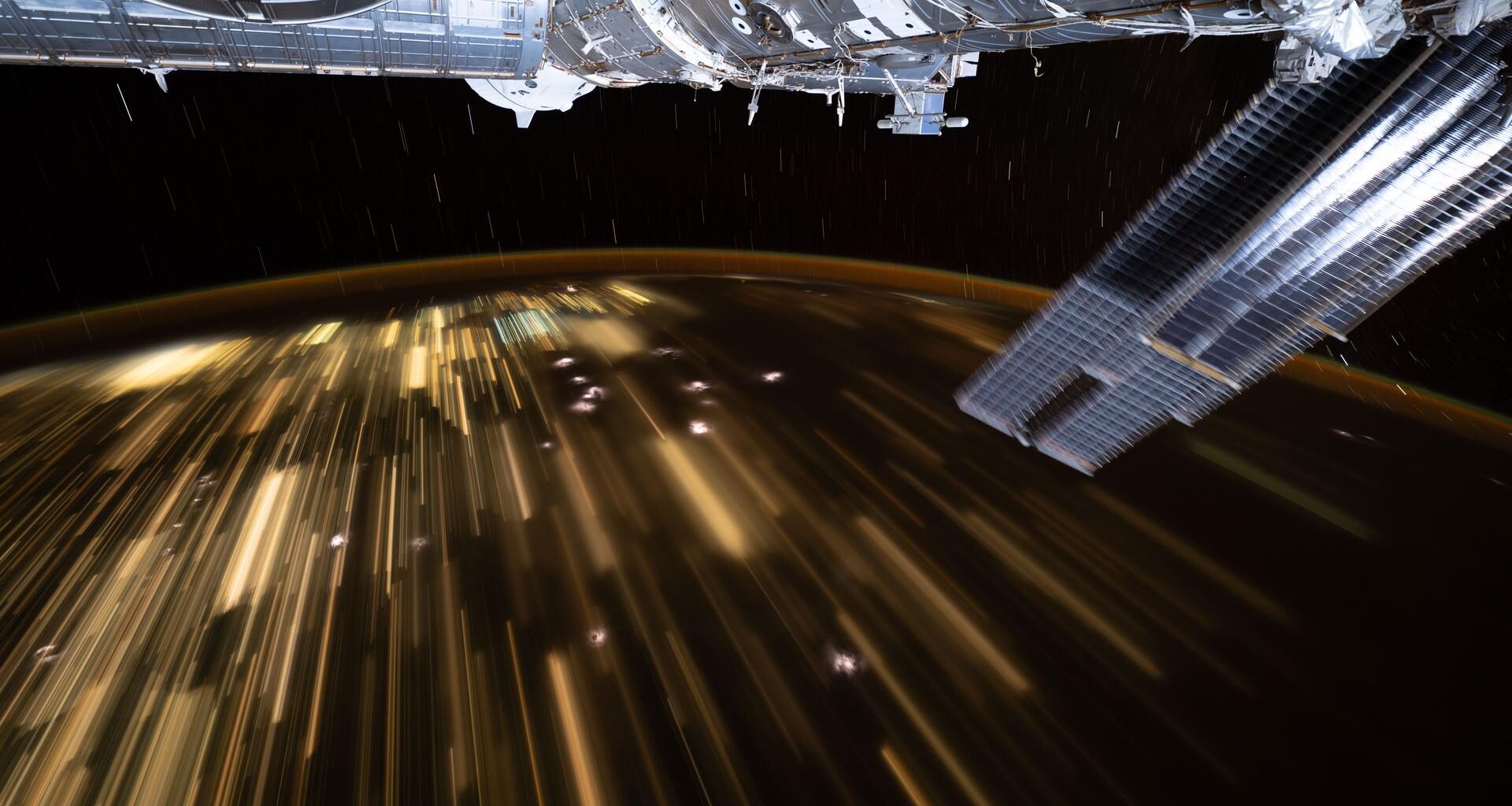 The warm city lights of Southeast Asia streak below the silvery U.S. segment of the International Space Station in this 30-second exposure from the orbital outpost as it soared 259 miles above China at approximately 10:39 a.m. local time. Near the top center, is the partially obscured SpaceX Dragon spacecraft that docked to the Harmony module's forward port carrying NASA's Crew-11 mission.