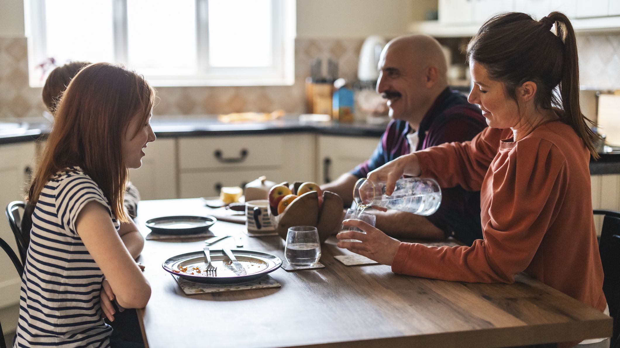 Family sits at table with a woman pouring water from a carafe into a glass