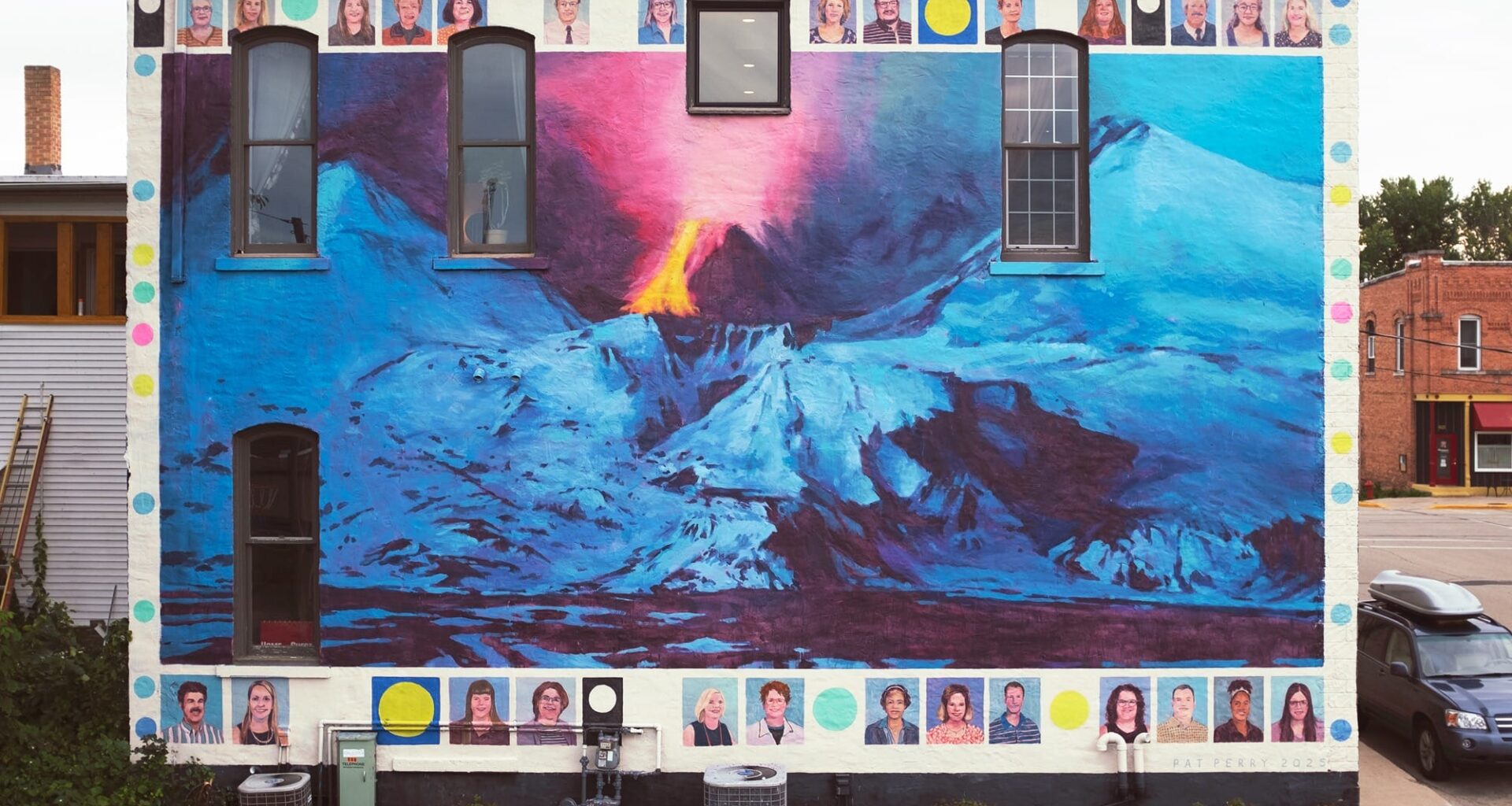a mural by Pat Perry of an exploding volcano and snow-covered mountains. a top and bottom border features portraits of schoolteachers