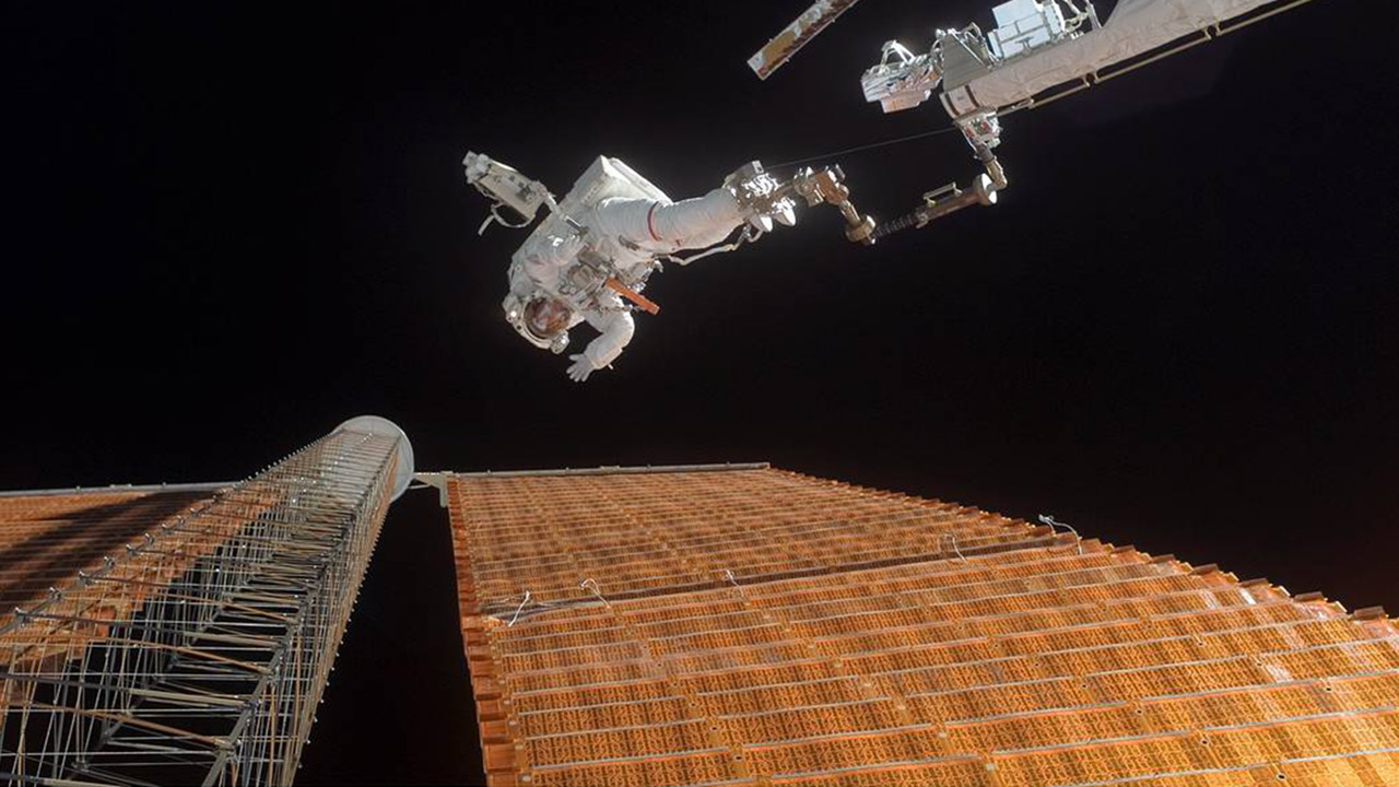 An astronaut in space beside a massive solar panel