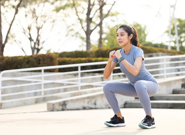Beautiful fitness asian woman doing squat sit up exercise workout at sport stadium. Attractive female warming up body training wearing sportswear. Healthy and active lifestyle concept.