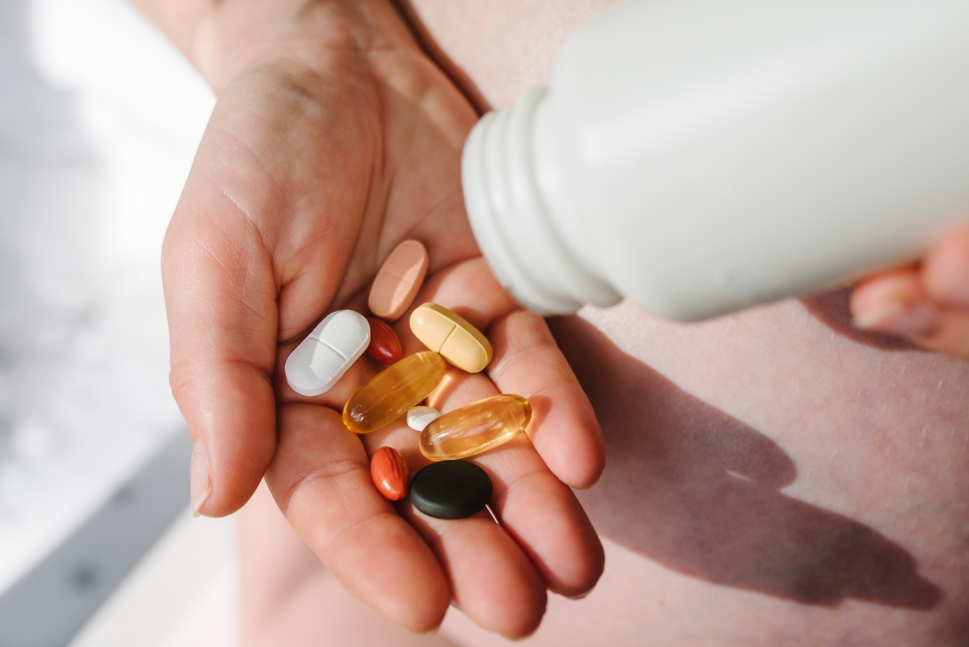 Closeup photo of supplements with a white bottle. Woman take omega 3, multivitamins, vitamins B, C, D, collagen tablets, probiotics, iron capsule. Girl hold vitamins daily. Top view.