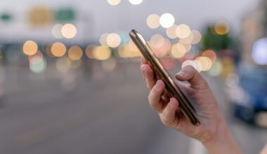 Close-up image of female hands using smartphone at night on city shopping street, searching or social networks concept, Side view shot of hipster woman typing an sms message to her friends at night city street, bokeh lights. chatting with friends at social networks via cellphone outdoor