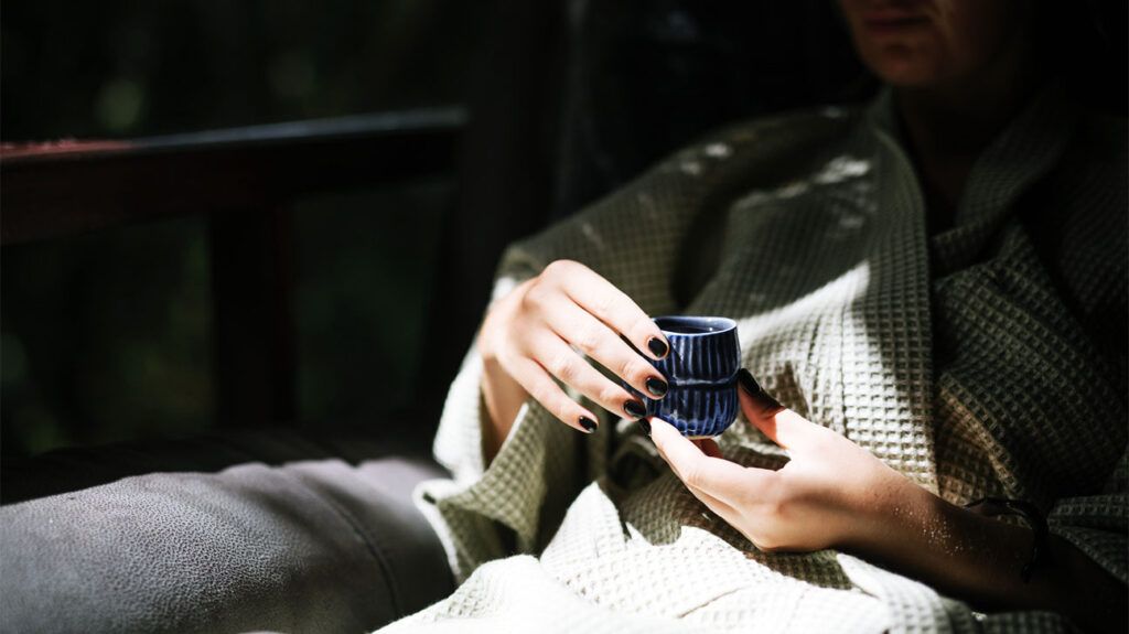A person holding a cup of green tea, a part of a green Mediterranean diet, as their hands are illuminated by sunlight
