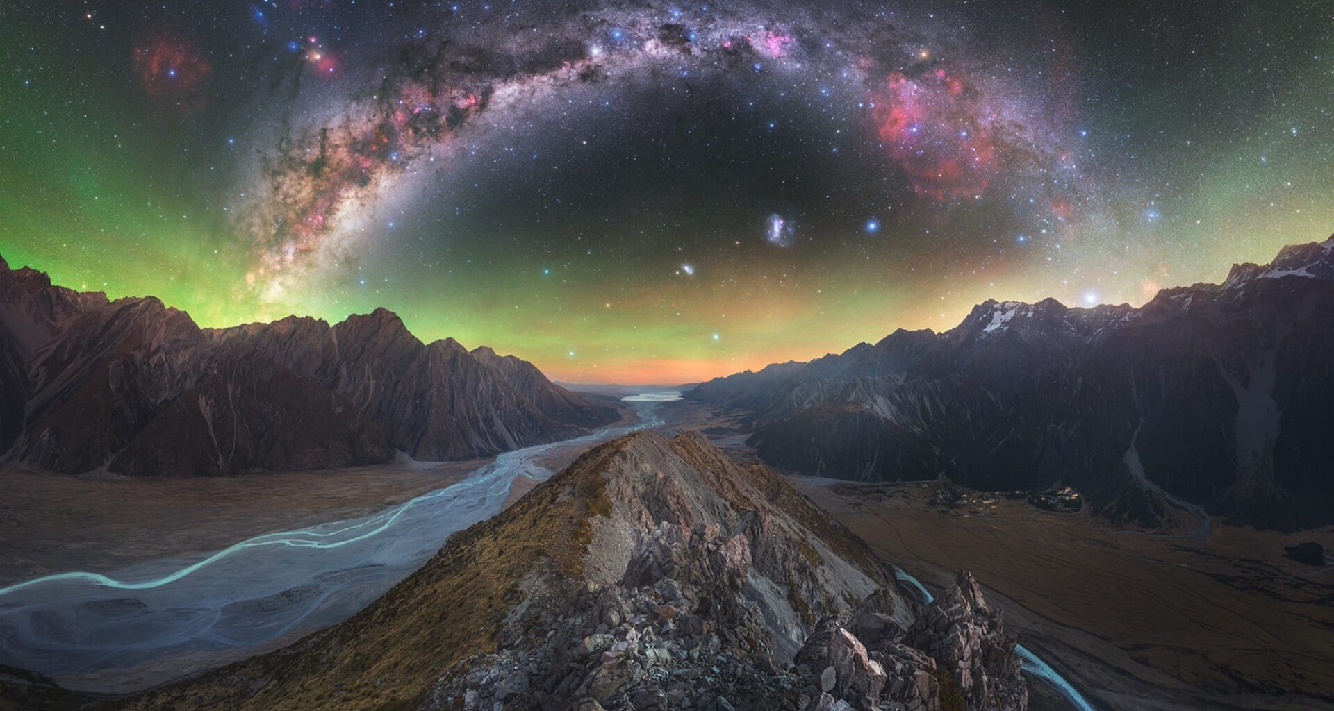 a dramatic wide-angle photo of a rocky landscape with aurora borealis and the Milky Way above