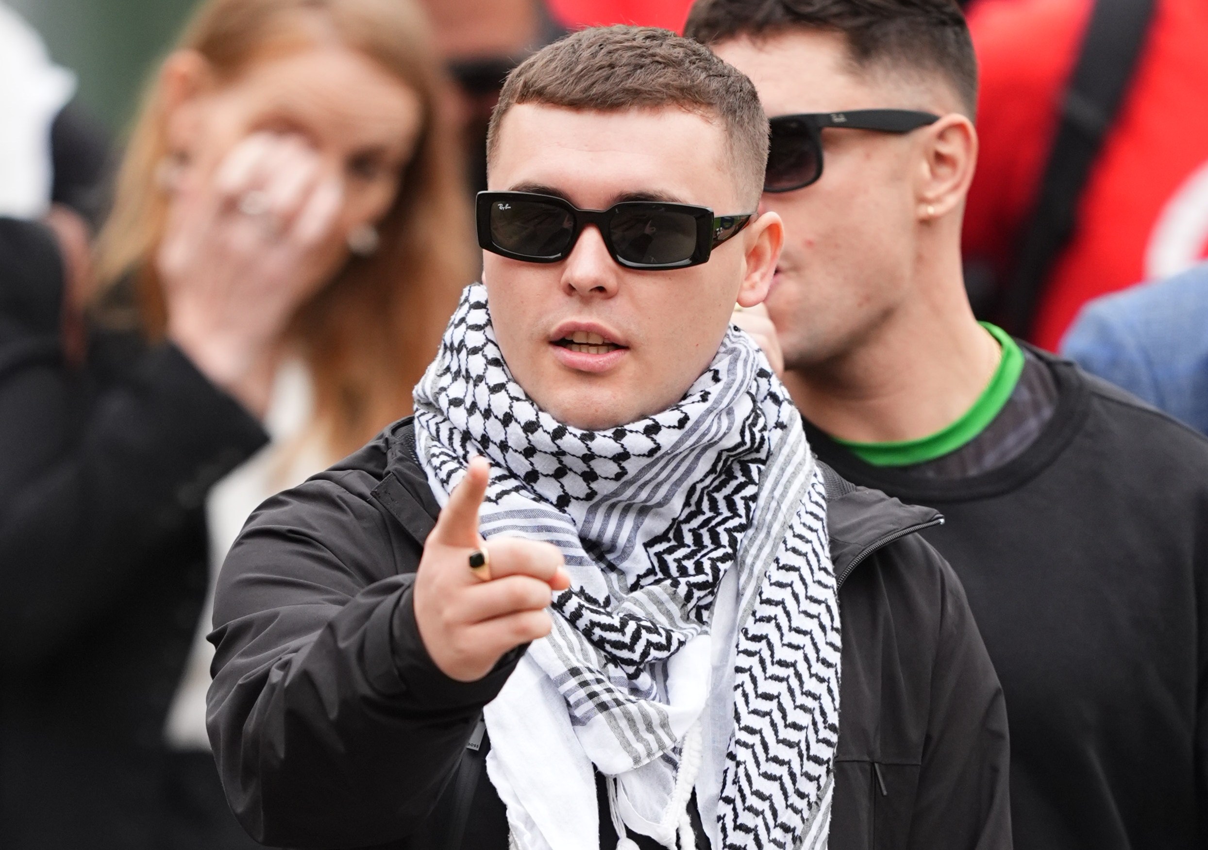 Liam Og O hAnnaidh, wearing sunglasses and a keffiyeh, points his finger outside Woolwich Crown Court.
