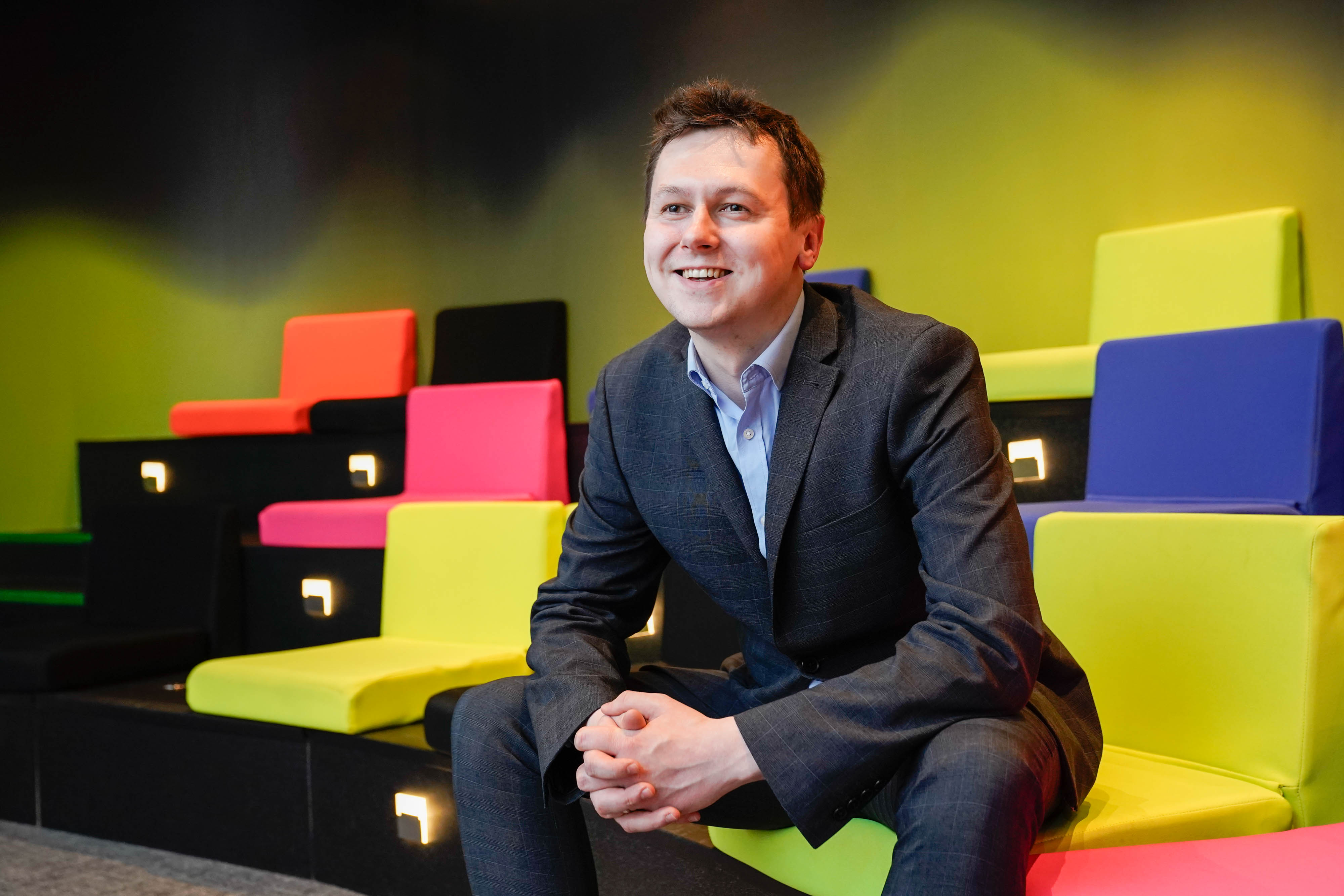 Adam Harris, CEO of AsIAm, sits in front of brightly colored cushions.