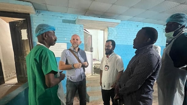 Five men speak to each other. Two men are hearing medical protective equipment