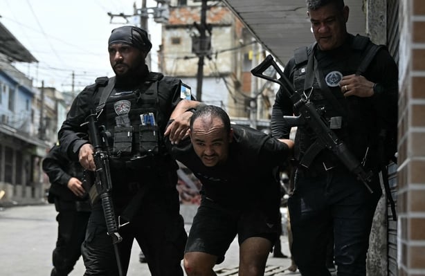A suspect is escorted by police officers after being arrested during the Operacao Contencao (Operation Containment) at the Vila Cruzeiro favela, in the Penha complex, in Rio de Janeiro, Brazil, on October 28, 2025. At least 2,500 agents took part in an operation to arrest drug traffickers from the C