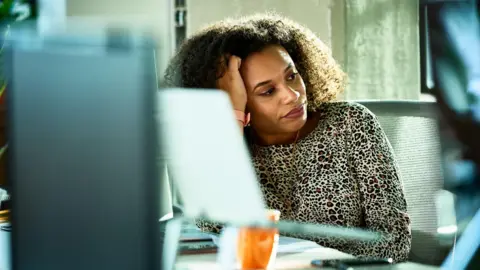 Getty Images A woman looking distant and stressed at her desk in the office