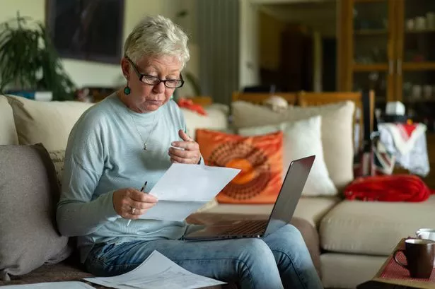 An elderly lady is looking at her bank statements worrying about her pension and the rising cost of living, sitting on a couch in her living room