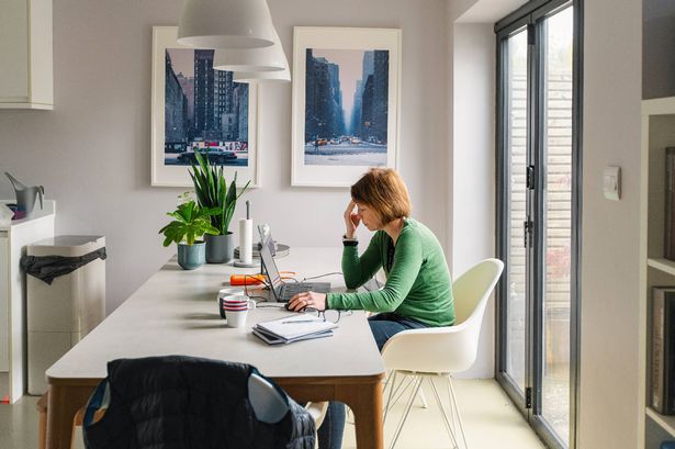 A stressed mature woman works from her dining table at home