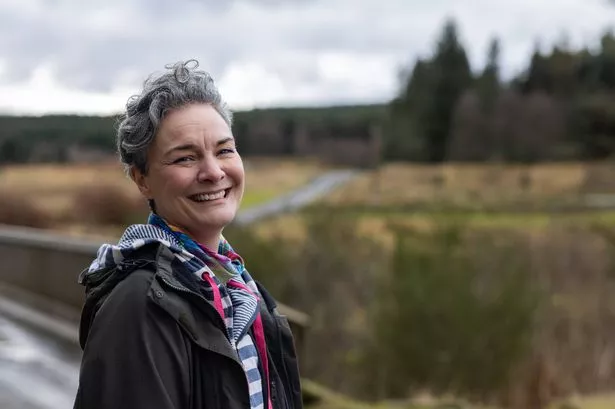 Woman standing outdoors while on a walk in Northumberland, North East England. She is relaxing in the countryside, taking care of her health. She is looking at the camera, laughing.