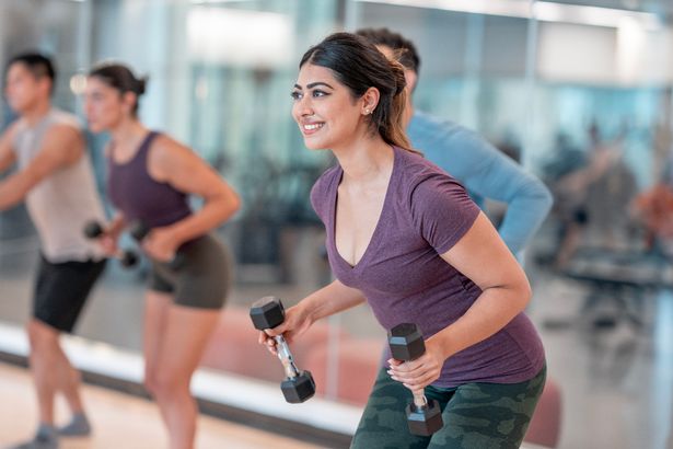Energetic group performing fitness exercises with dumbbells in a bright and modern gym environment.