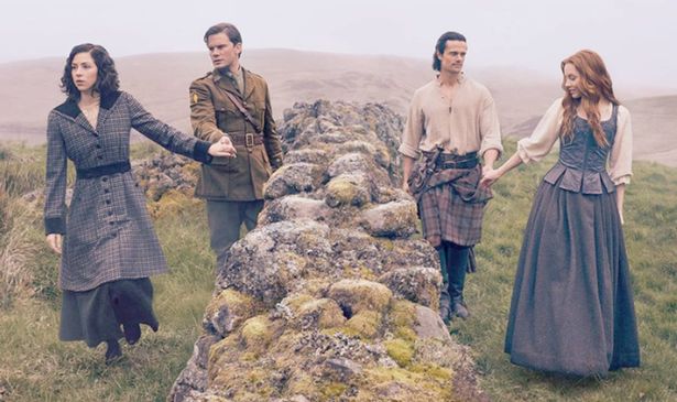 Two couples walk on either side of a wall in a field 